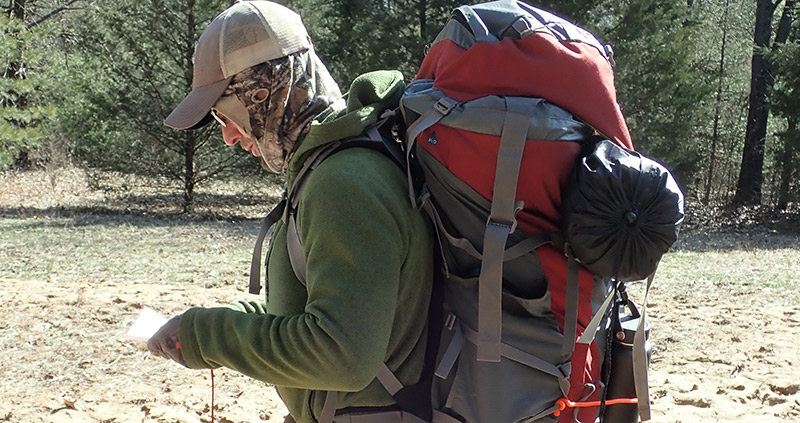 A man wearing a hat and carrying a backpack stands in Sand Ridge State Forest